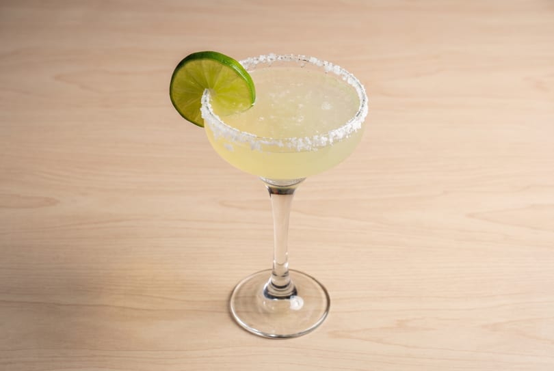 Margarita cocktail in a glass with a salted rim and lime wedge on a wooden table.