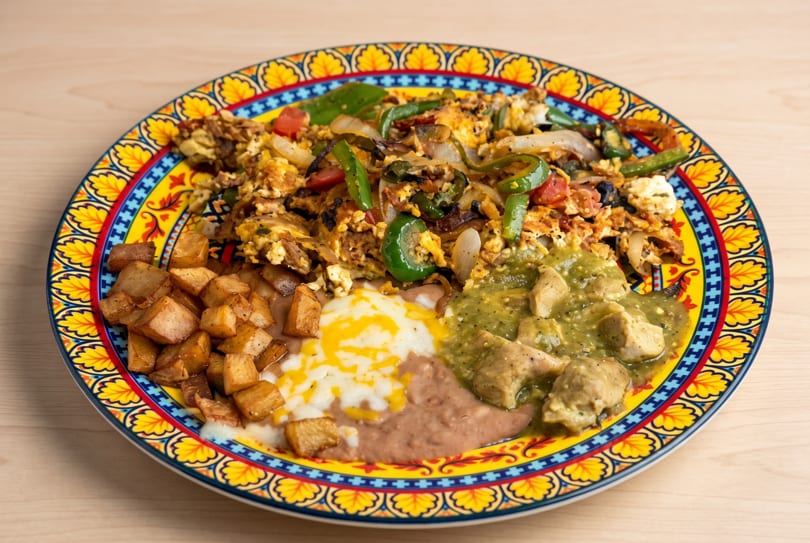 Vibrant plate of scrambled eggs, potatoes, refried beans, and green chile chicken.