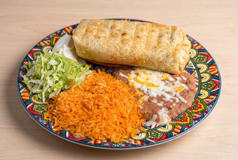Burrito, Mexican rice, refried beans with cheese, shredded lettuce, and sour cream on a vibrant plate.