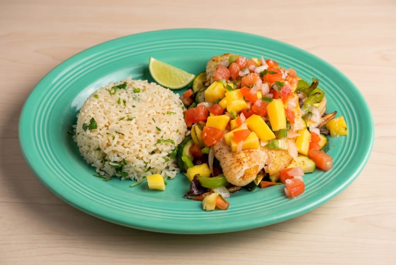 Seared fish with vibrant mango salsa, cilantro rice, grilled vegetables, and a lime on a teal plate.
