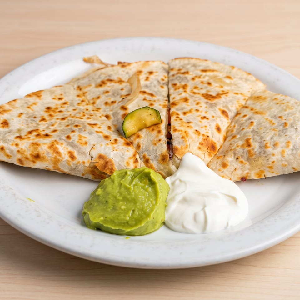 A quesadilla cut into four triangles, served with guacamole, sour cream, and a zucchini slice.