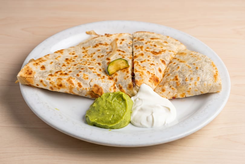 Quesadilla cut into four pieces, served with guacamole, sour cream, zucchini, and onion.