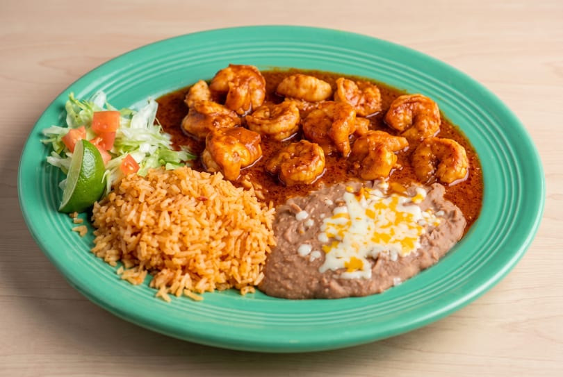 Shrimp in red sauce with rice, refried beans, and a side salad on a teal plate.